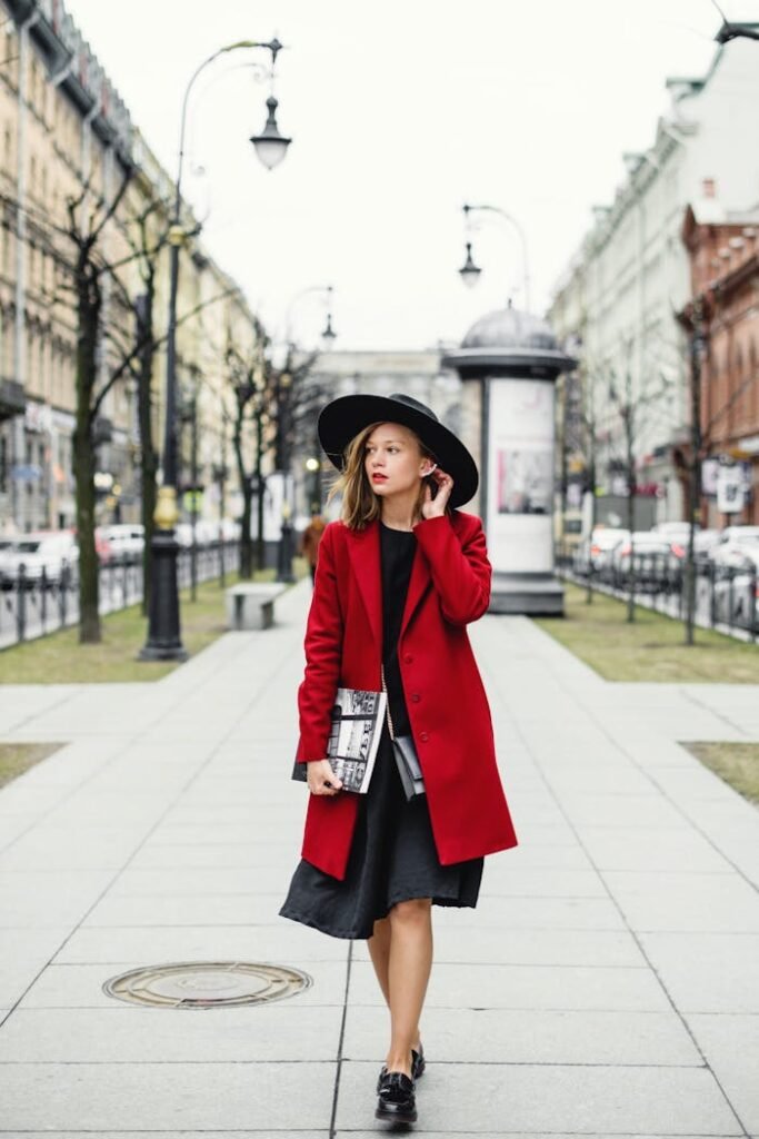 Fashionable woman in a red coat and black hat strolls through an urban street.