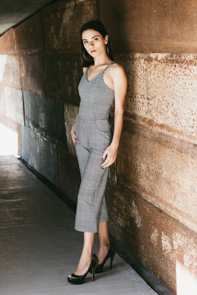 Elegant woman posing by textured wall in stylish outfit.